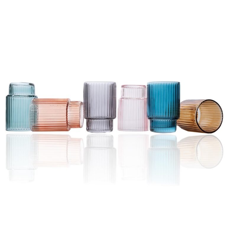 Six colorful, ribbed glass tumblers arranged on a reflective white surface